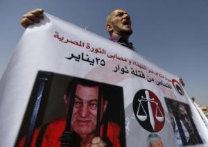 A man whose relatives were killed during the 2011 Egyptian revolution, holds a banner with pictures of former Egyptian President Mubarak as he shouts slogans outside the police academy on the outskirts of Cairo