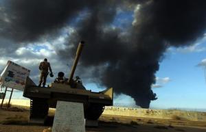 A member of the Libyan army stands on a tank as heavy black smoke rises from the city's port in the background after a fire broke out at a car tyre disposal plant during clashes against Islamist gunmen in the eastern Libyan city of Benghazi