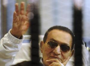 Former Egyptian President Hosni Mubarak waves to his supporters inside a cage in a courtroom at the police academy in Cairo